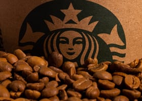 A detailed image of roasted coffee beans placed in front of a cardboard cup featuring a green logo.